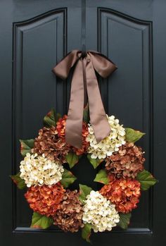 a wreath is hanging on a door with a brown ribbon and flowers are in the center