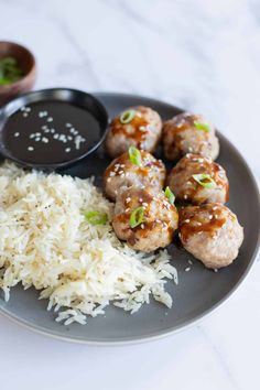 meatballs, rice and dipping sauce on a black plate with a white tablecloth