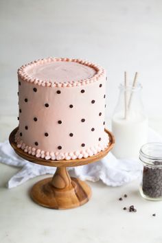 a pink cake sitting on top of a wooden stand next to a bottle of milk