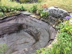 an outdoor pool is covered with black tarp and surrounded by greenery, shrubs and flowers