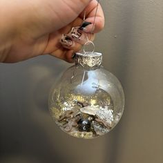 a hand holding a clear glass ornament with gold and silver decorations on it