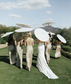 four bridesmaids walking in the grass with umbrellas over their heads