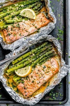 salmon and asparagus wrapped in foil on a baking sheet with lemon wedges