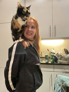 a woman is holding a cat on her shoulders in the kitchen while smiling at the camera