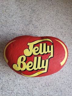 a red rock with the word jelly belly on it sitting on a gray floor next to a yellow sticker