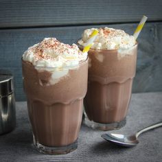 two glasses filled with ice cream and topped with whipped cream, one has a straw in it