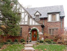 a large brick house with a red door and white trim on the windows, surrounded by green grass and trees