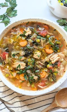 a white bowl filled with chicken and vegetable soup next to a wooden spoon on a striped towel