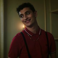 a man in a red shirt and suspenders smiles at the camera with a lit candle behind him