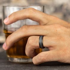 a man's hand with two wedding bands on his wrist next to a glass of whiskey