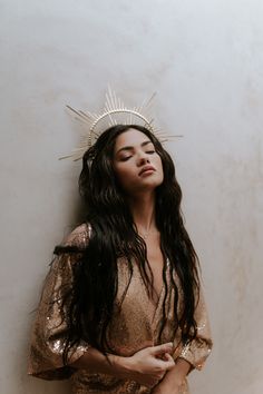 a woman with long hair and a crown on her head standing in front of a wall