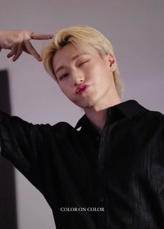 a man with blonde hair and black shirt holding his hand up to his head while standing in front of a mirror