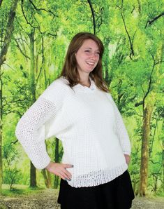 a woman standing in front of a painting wearing a white sweater and black skirt with her hands on her hips