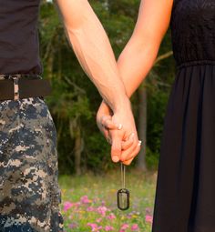 two people holding hands while standing next to each other in front of flowers and trees