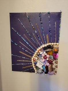 a purple wall hanging with beads and necklaces on it's side, next to a white wall