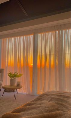 a bedroom with sheer curtains and a chair in the foreground, overlooking an ocean at sunset