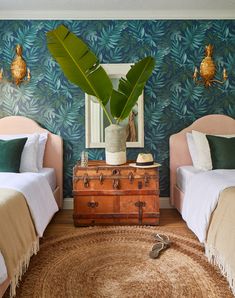 two beds in a room with blue and green wallpaper, one has a trunk on the floor