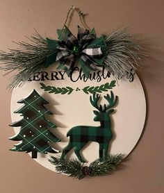 a christmas sign hanging from the side of a wall next to evergreen trees and pine cones