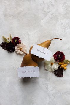 two pears with name tags attached to them sitting next to flowers on a white surface