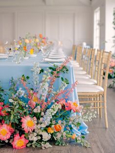 the table is set with blue linens and colorful floral centerpieces on it