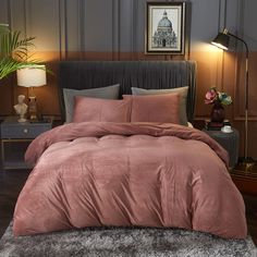 a bed with pink comforter and pillows in a room next to a lamp on a table