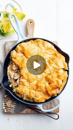 a skillet filled with food sitting on top of a wooden cutting board next to utensils