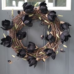 a wreath with black flowers is hanging on the front door's gray door frame