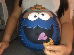 a pregnant woman with cookie cookies on her stomach holding a cookie in her hand while sitting down