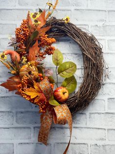 an autumn wreath with apples and leaves on a white brick wall next to a brown ribbon