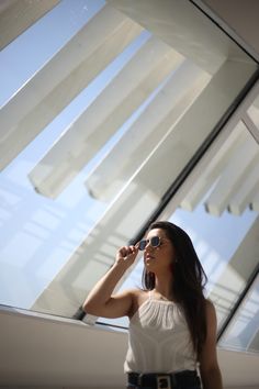 a woman standing in front of a window with her hand on her hip and looking up at the sky