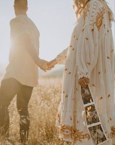 a man and woman holding hands in the middle of a field with sun shining on them