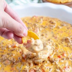 a hand dipping a tortilla chip into a bowl of cheese dip