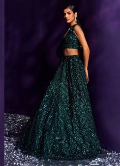 Introducing the exquisite Emerald Green Sequins Embroidered Lehenga Set, a masterpiece of elegance and sophistication. Crafted from delicate net fabric, this flowing green lehenga is meticulously adorned with tonal multi-cut sequins, crystals, and bugle beads, creating a mesmerizing shimmer that captivates with every movement. The intricate embroidery adds depth and richness, enhancing the luxurious appeal of the ensemble. Paired with a matching V-neckline blouse that perfectly balances the modern and traditional elements. Completed with an embellished dupatta for a cohesive, stunning look. Ideal for the bride or bride-to-be, especially for Cocktail or Sangeet nights, this lehenga set ensures you will be the center of attention, radiating timeless allure and unmatched opulence. Composition Green Lehenga, Embroidered Lehenga, Net Fabric, Green Sequins, Intricate Embroidery, Bugle Beads, Emerald Green, Lehenga, The Bride