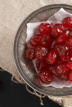 a glass bowl filled with cherries sitting on top of a table next to a piece of cloth