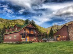 a large wooden house sitting in the middle of a lush green field under a cloudy sky