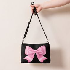 Jump into the pink bow aesthetic and coquette trend with this versatile pink bow crossbody bag with a black background. It has a modern and playful feel, which makes this handbag a great accessory and a perfect gift for every occasion. It's made of premium faux leather and features dark gray hardware. Thanks to the zip-top closure and multiple inside pockets, you can keep your essentials secure and organized. Transform this crossbody bag with removable wrist and shoulder straps to style it for d Pink Shoulder Bag With Bow, Cute Pink Shoulder Bag For Evening, Cute Pink Evening Shoulder Bag, Black Party Bags With Bow Detail, Pink Shoulder Bag With Bow For Everyday Use, Cute Black Shoulder Bag With Detachable Strap, Black Rectangular Bag With Bow, Black Bow Shoulder Bag For Party, Pink Bow Bag For Daily Use