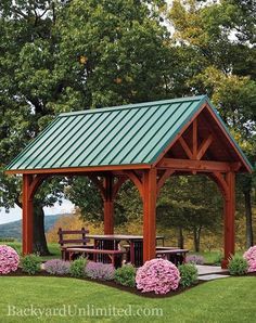 a wooden gazebo sitting in the middle of a lush green field with pink flowers