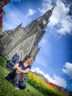 a woman sitting on the ground in front of a tall building with a clock tower