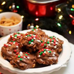 chocolate covered cookies with sprinkles on a white plate next to a christmas tree