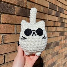 a hand holding up a crocheted cat with sunglasses on it's face