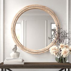 a round mirror on the wall above a table with flowers in vases and books