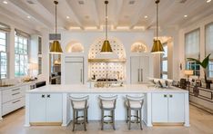 a large kitchen with white cabinets and gold pendant lights hanging from the ceiling, along with bar stools