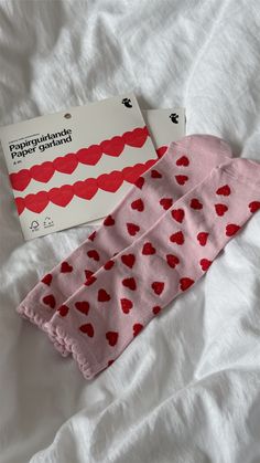 two pairs of pink socks with hearts on them sitting on a white sheet next to a book