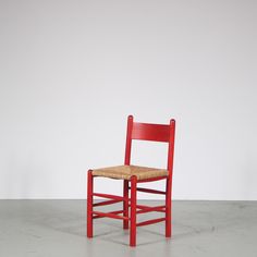 a red wooden chair with a woven seat and back rests against a plain white wall