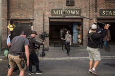 several people standing in front of a building with cameras on the street and one person holding a baseball bat