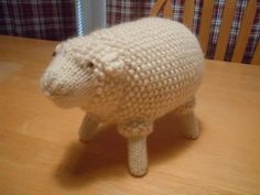 a crocheted sheep sitting on top of a wooden table next to a chair