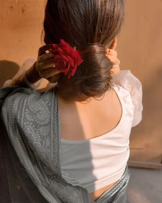 a woman with her back to the camera, wearing a white top and holding a red rose in her hair