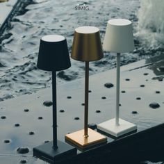 three lamps sitting on top of a table next to water