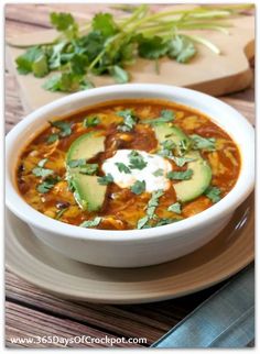 a white bowl filled with soup and topped with sour cream, avocado and cilantro