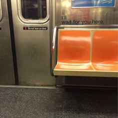 an orange seat on a subway train next to the door that says i'll wait for you here